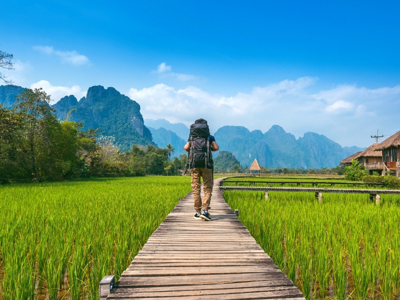 800 - Laos für Entdeckertourism-with-backpack-walking-on-wooden-path-vang-vieng-in-laos