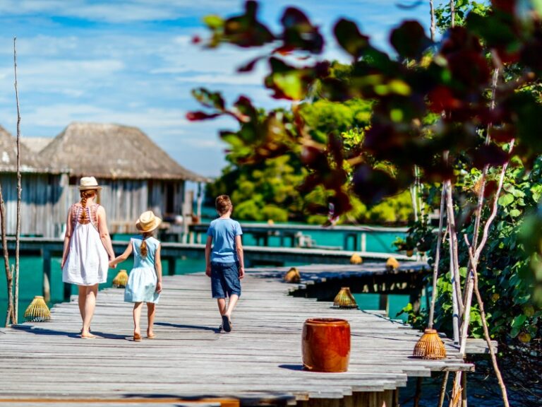 Back view of happy beautiful family walking on wooden jetty during summer vacation at luxury resort