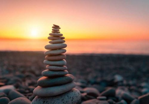 Stone pyramid on the background of sunset and sea on pebble beach symbolizing stability, zen, harmony and balance